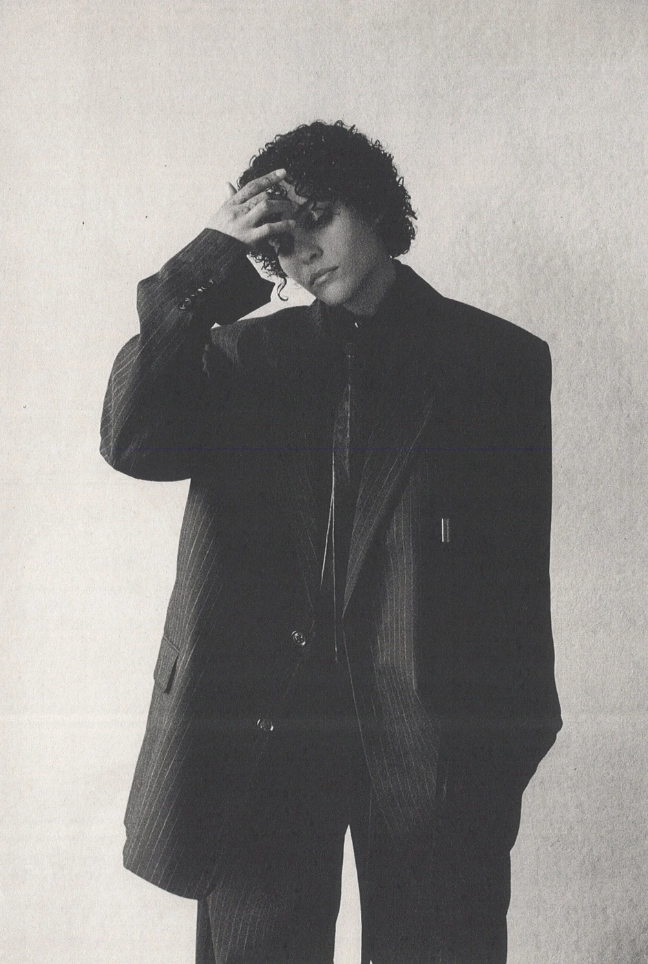 Model in oversized pinstripe suit jacket with hand on forehead against a textured light wall