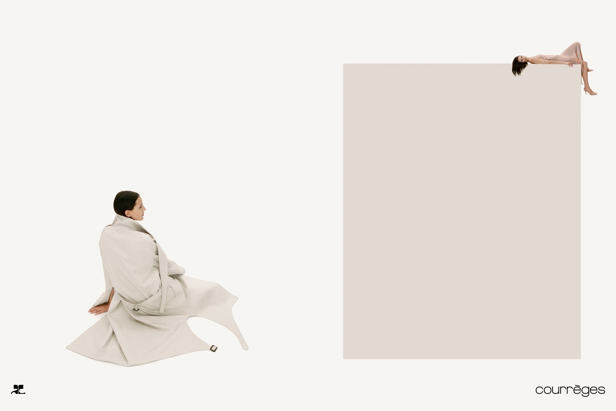 Model wrapped in a light beige coat seated on white background with a second model lying atop a large rectangular block