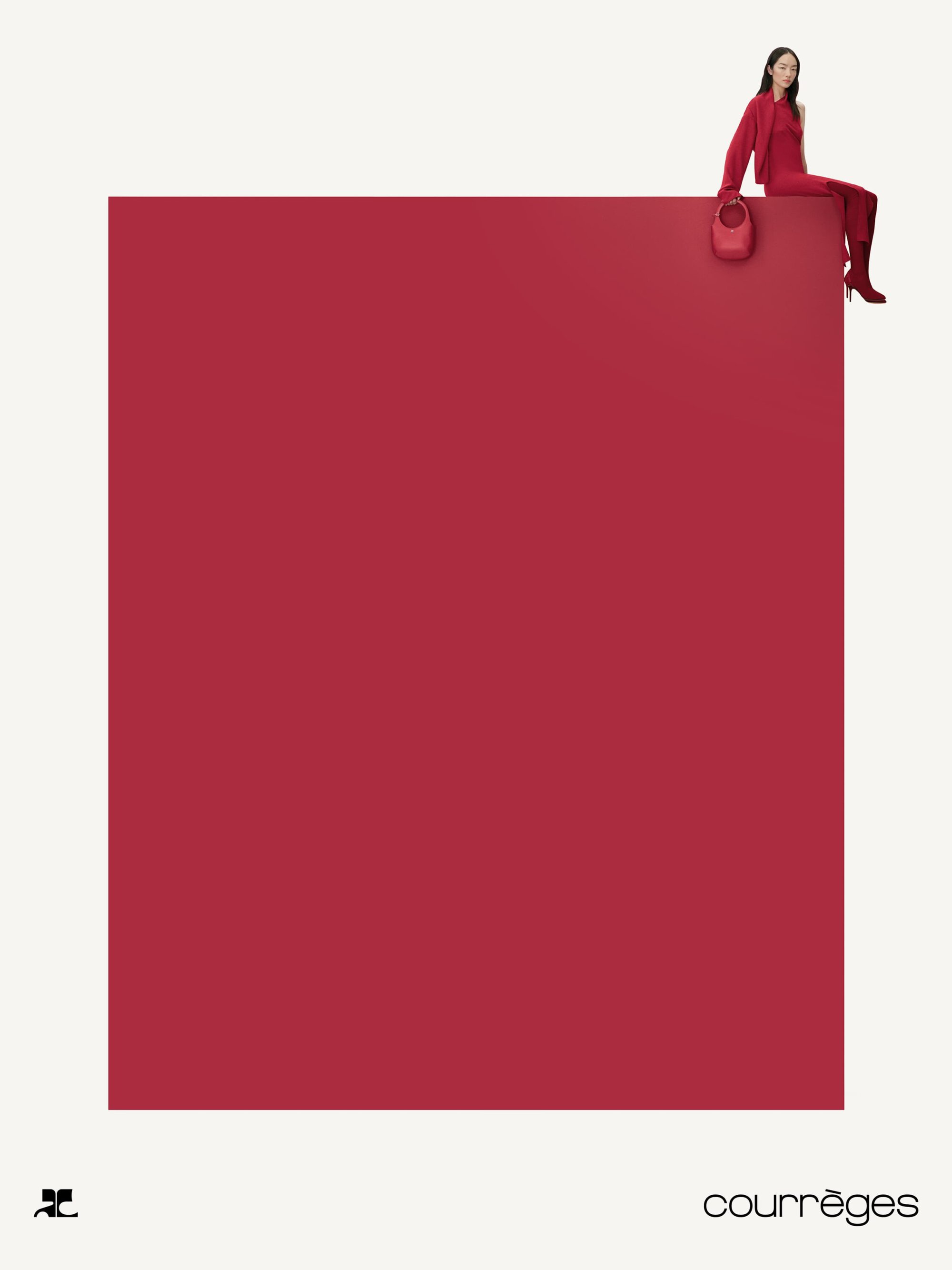 Model in red attire seated on the edge of a red monolithic block against a minimalist white background