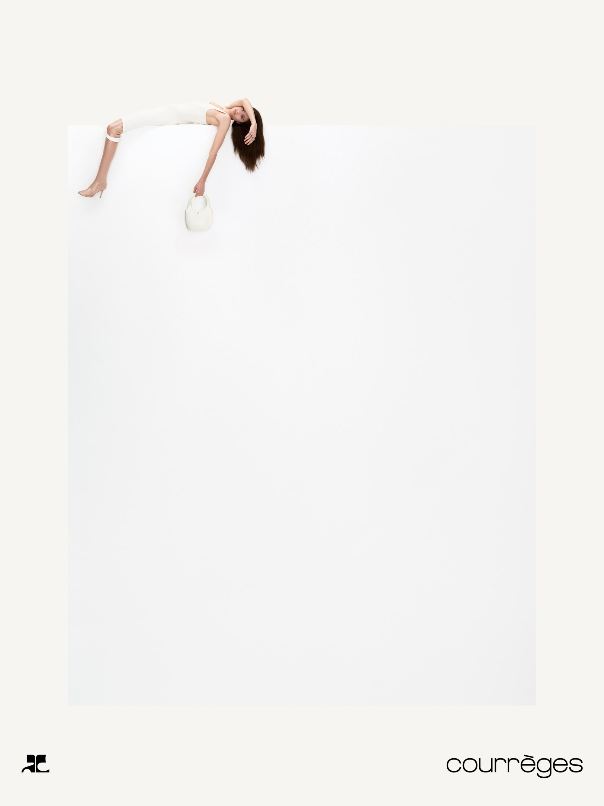 Model lying on edge of large white block holding handbag in Courreges Fall 2024 campaign