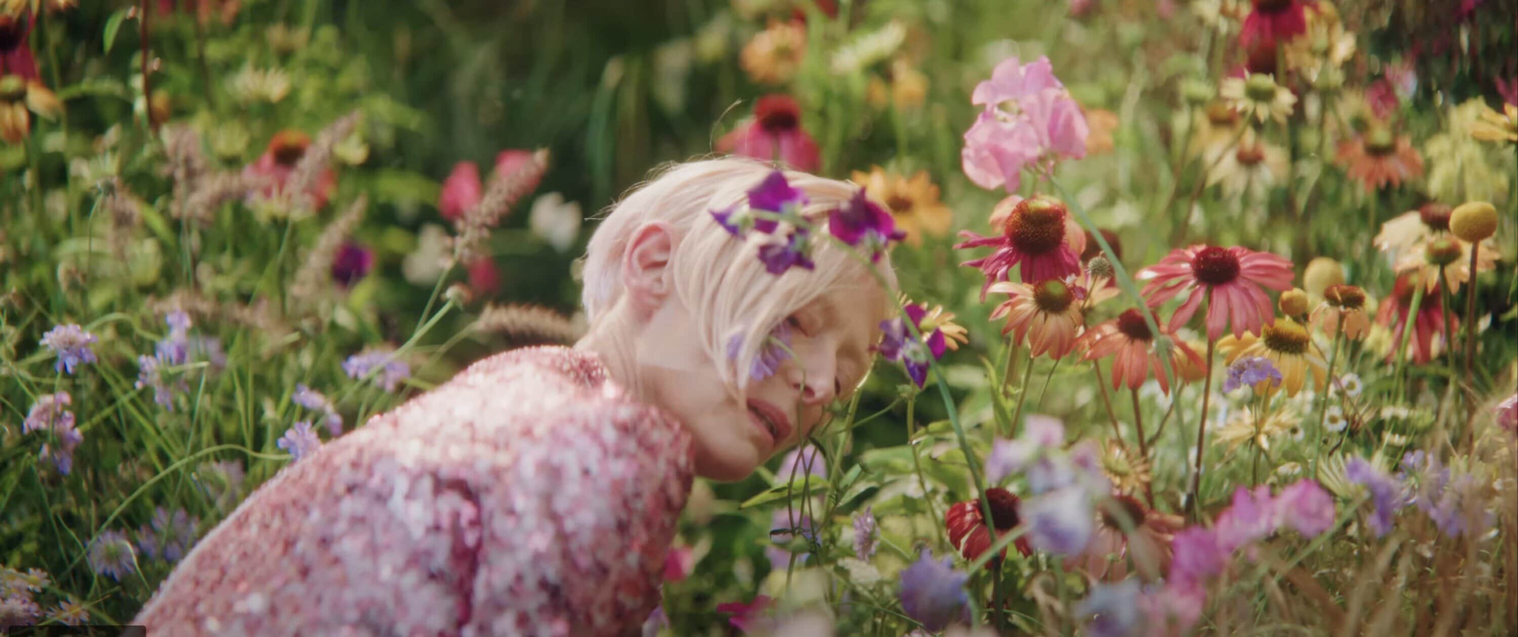 Tilda Swinton in a pink sequined top surrounded by vibrant wildflowers for the Delpozo Obertura ad campaign.