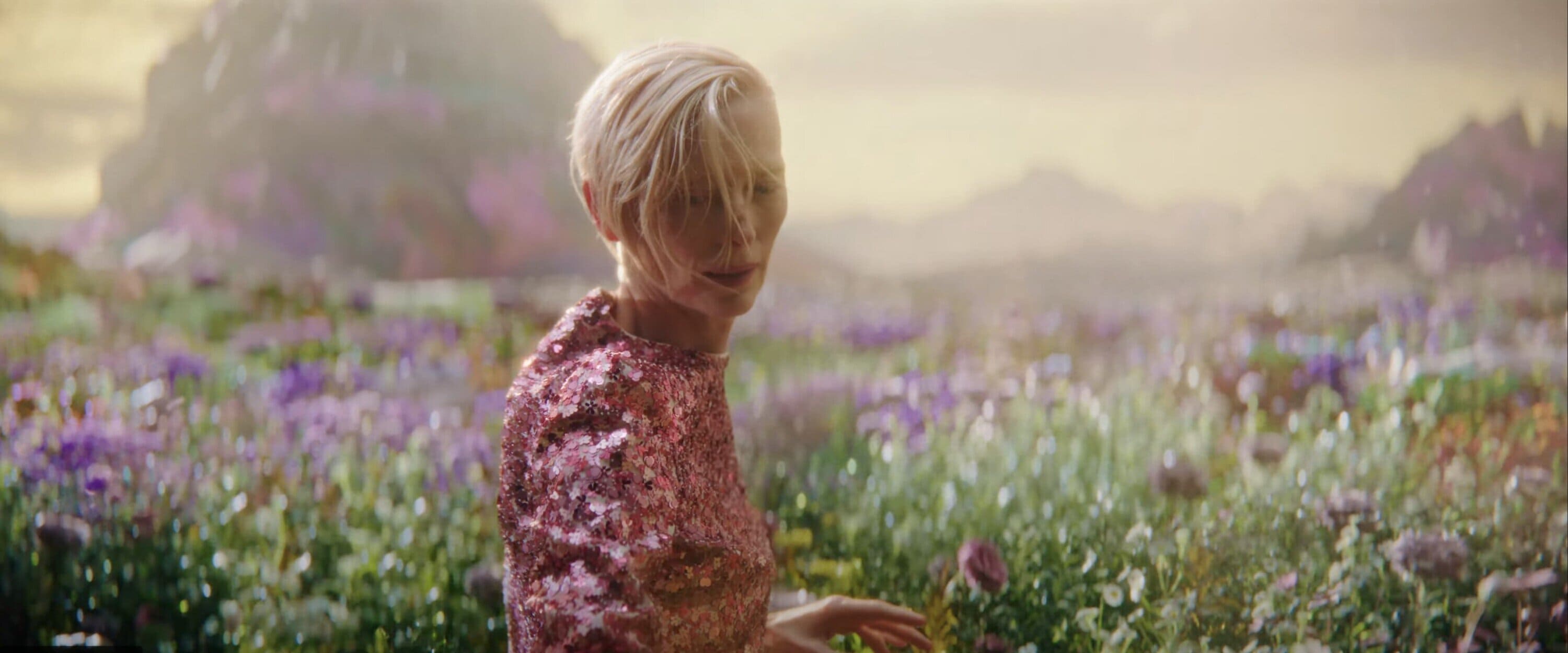 Tilda Swinton wearing a pink sequined top standing in a lush flowering meadow for Delpozo Obertura campaign