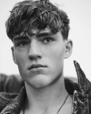 Close-up black and white portrait of a young male model wearing a denim jacket against a plain background