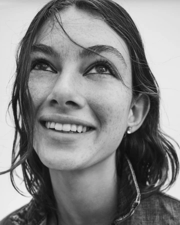 Close-up monochrome portrait of a smiling woman looking up, wearing a denim jacket against a light background.