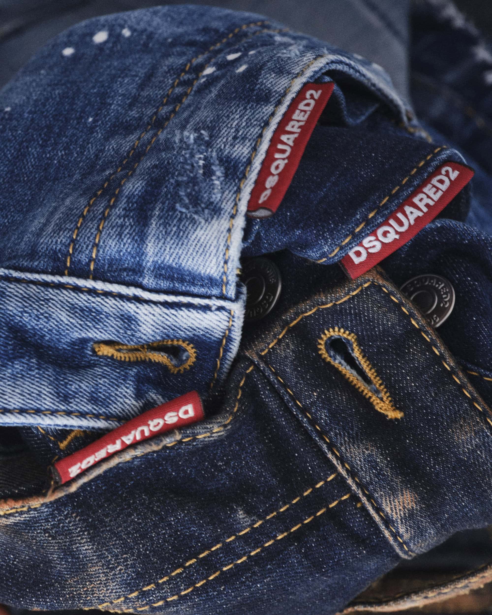 Close-up of stacked blue denim garments featuring visible brand tags and contrast stitching for Dsquared2