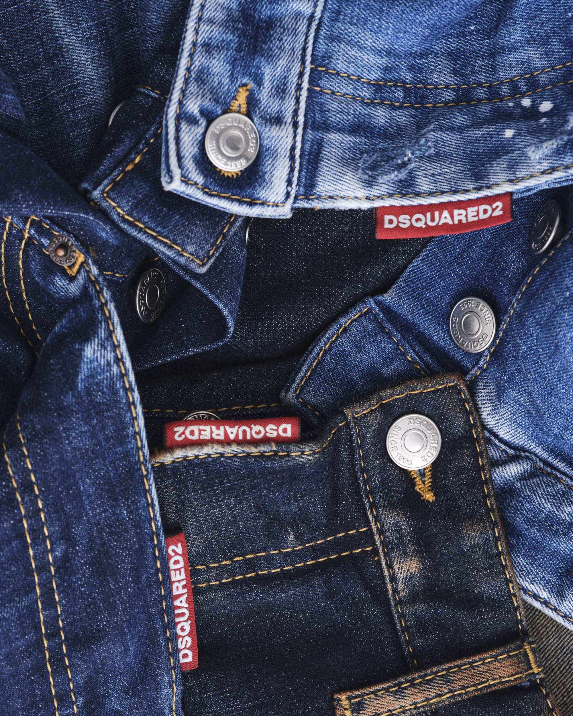 Close-up of layered denim jeans and jackets featuring metallic buttons and red DSQUARED2 branded tags for the Fall 2024 campaign.