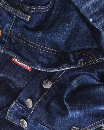 Close-up macro shot of dark blue denim jeans with orange topstitching, metallic buttons, and a red Dsquared2 label
