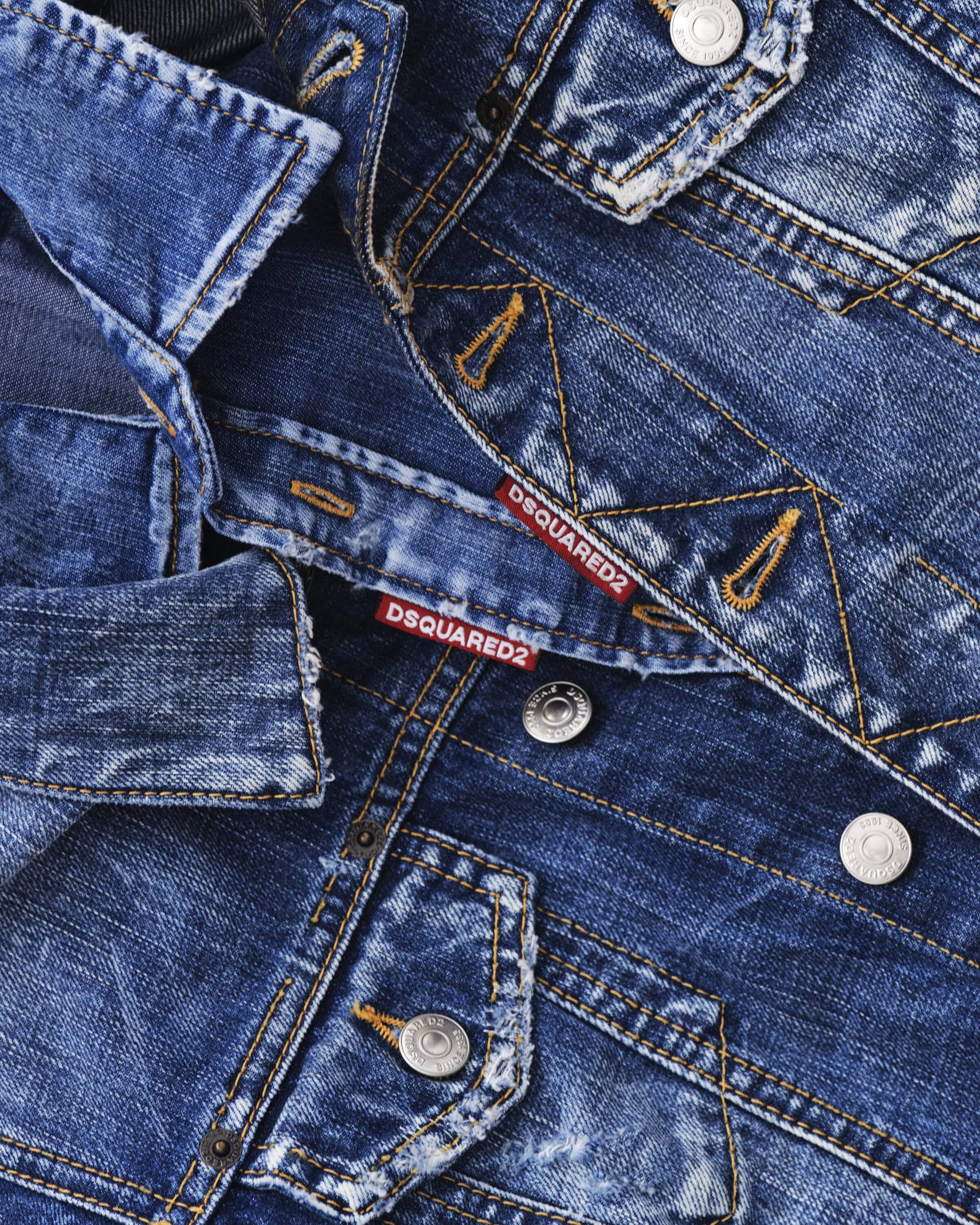 Close-up of blue distressed denim fabric with metal buttons and red Dsquared2 labels