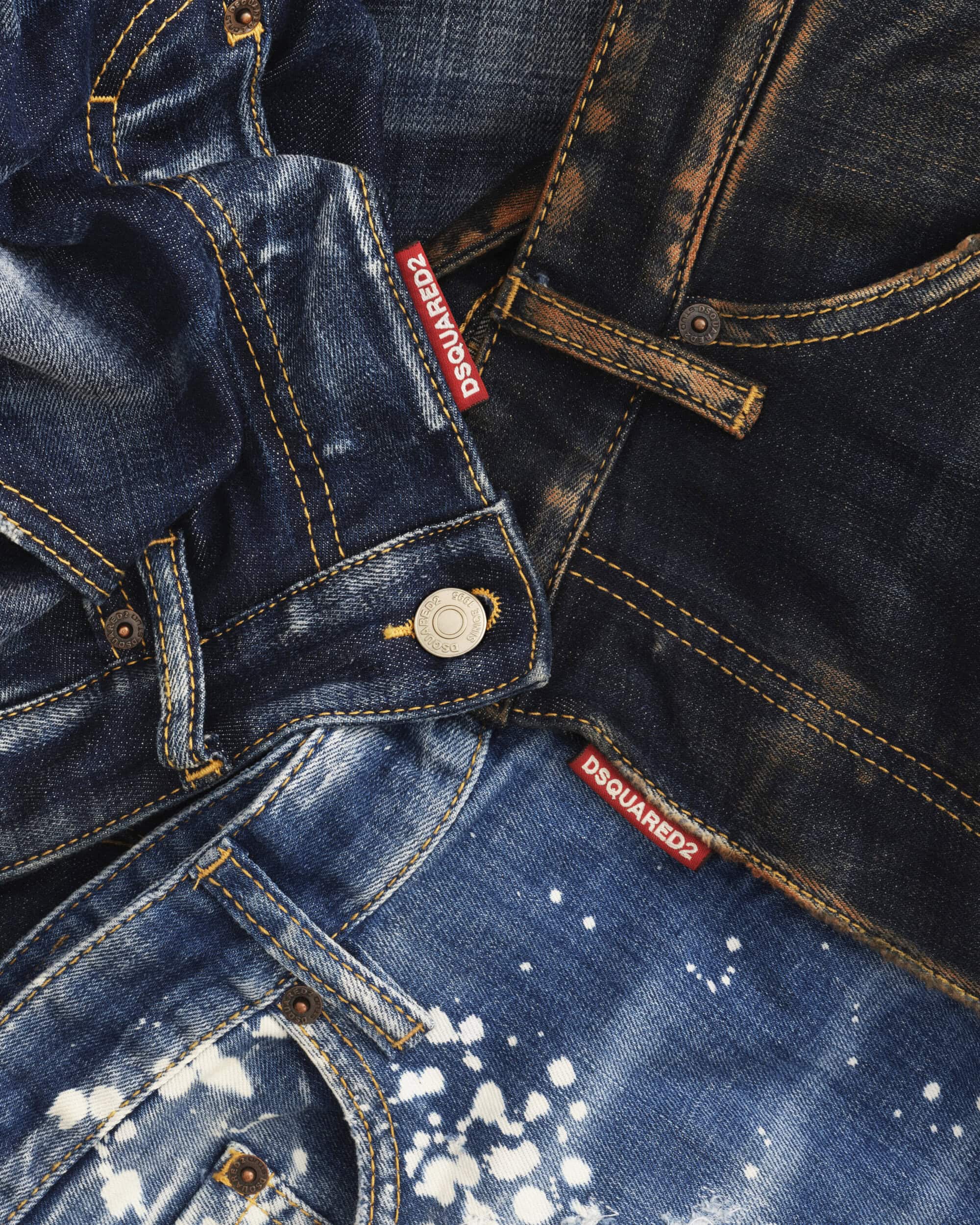 Close-up of layered denim jeans featuring contrasting washes, distressed textures, and visible Dsquared2 branded red labels.