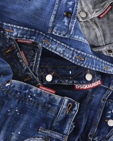 Close-up of stacked blue and grey denim jeans with contrast topstitching, metal buttons, and Dsquared2 logo labels.