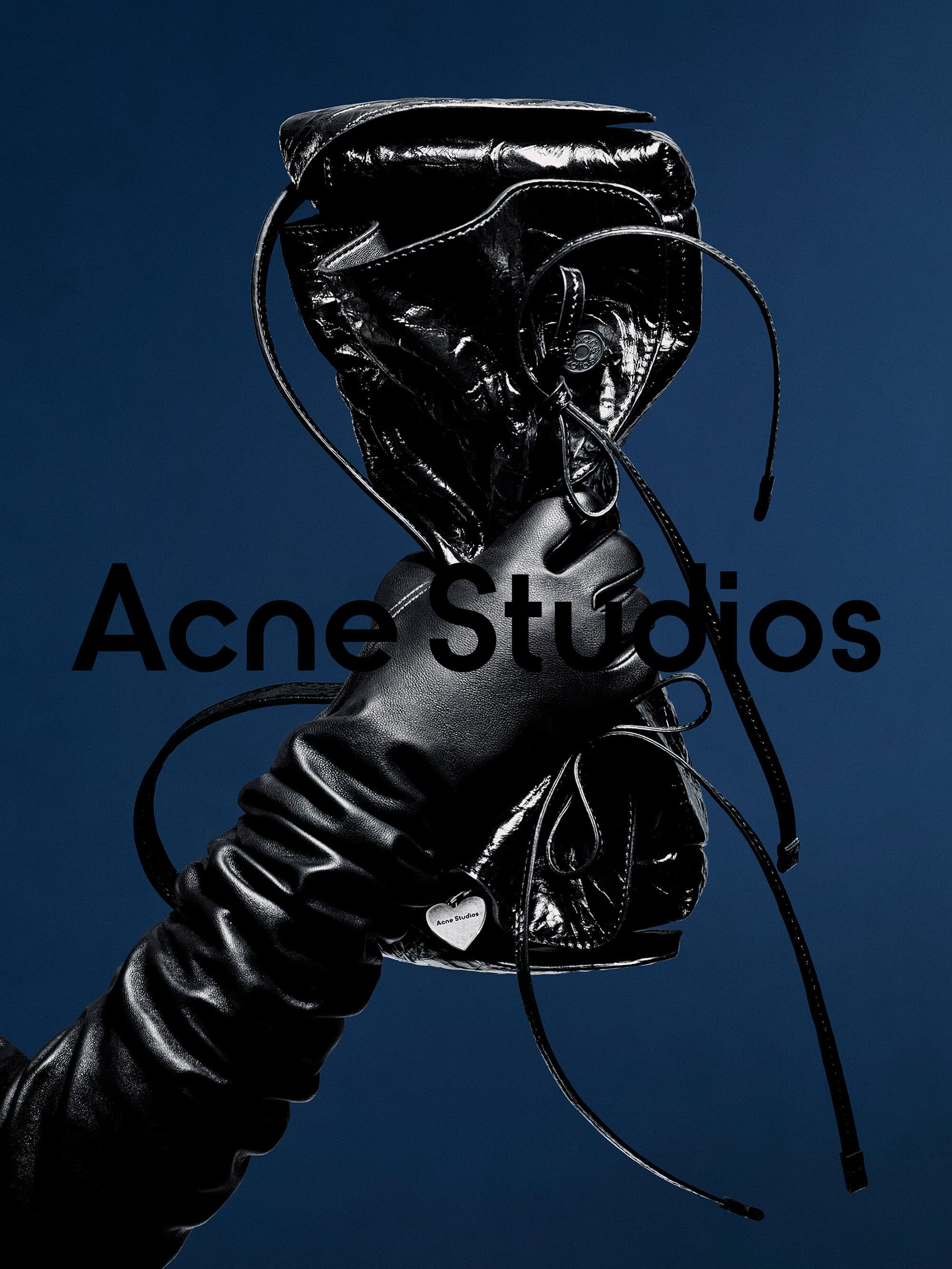 Gloved hand holding a shiny black leather bag against a dark blue background with brand text