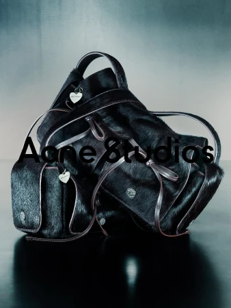 Stacked dark textured leather handbags with heart charms against a gradient background for Acne Studios