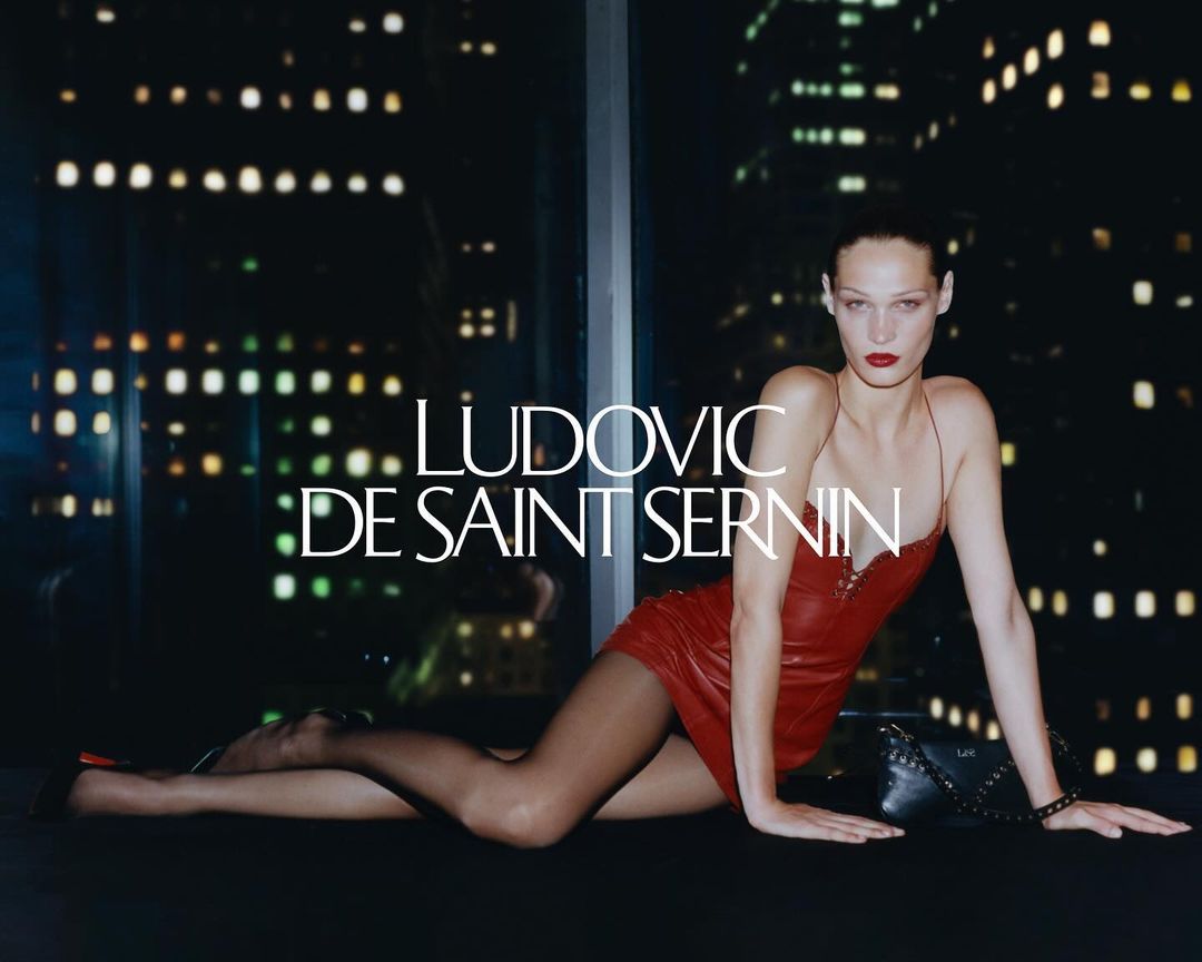 Model wearing a red leather dress posing against a night cityscape window for Ludovic de Saint Sernin fall 2024 campaign