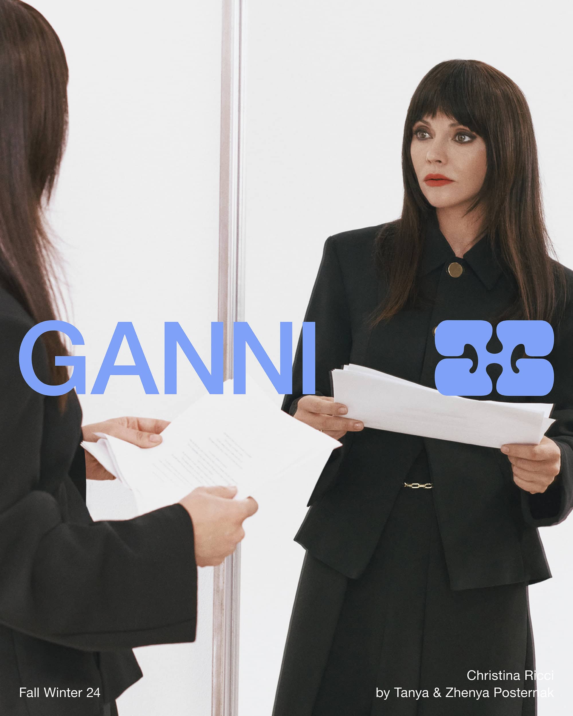 Christina Ricci reflected in a mirror holding papers wearing a black blazer for Ganni