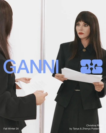 Christina Ricci reflected in a mirror holding papers wearing a black blazer for Ganni