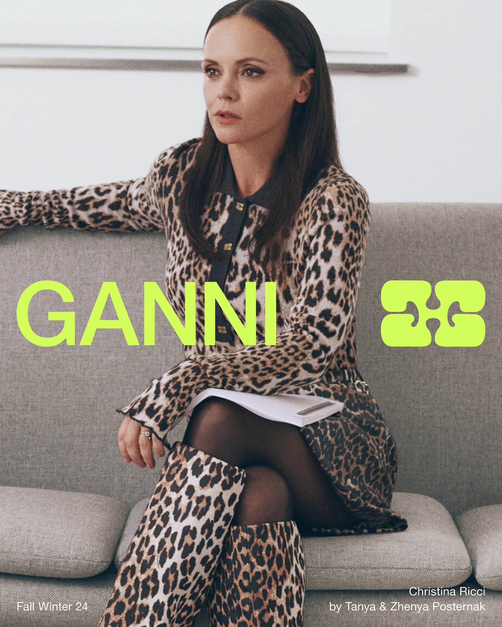 Christina Ricci seated on a grey sofa wearing a leopard print dress and matching boots for Ganni Fall 2024 campaign