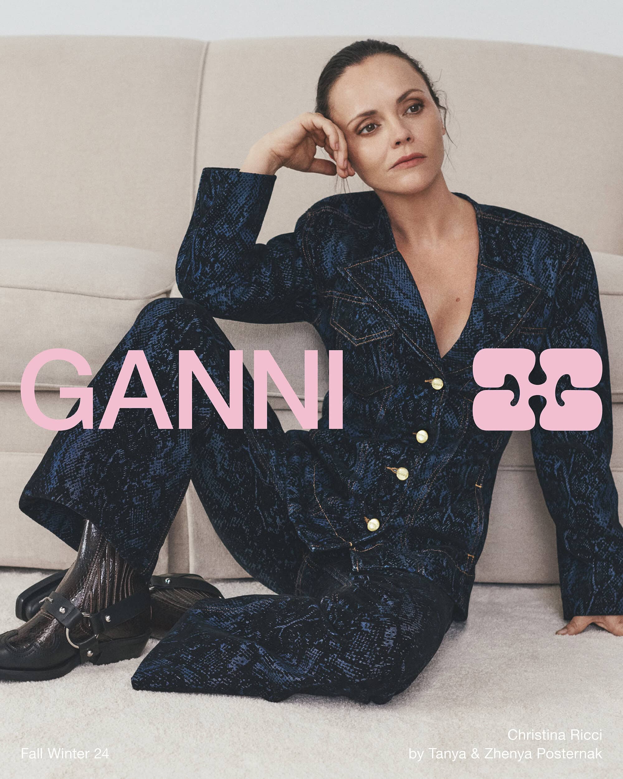 Christina Ricci wearing a patterned dark blue suit seated against a neutral upholstered sofa for Ganni