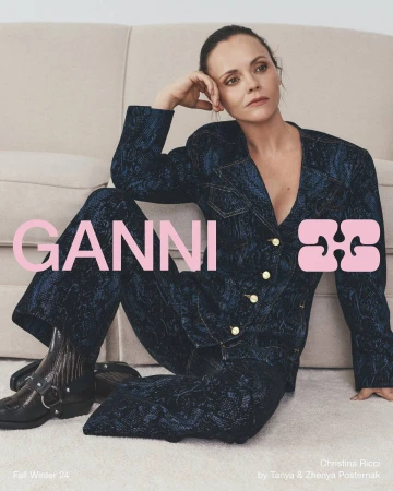 Christina Ricci wearing a patterned dark blue suit seated against a neutral upholstered sofa for Ganni