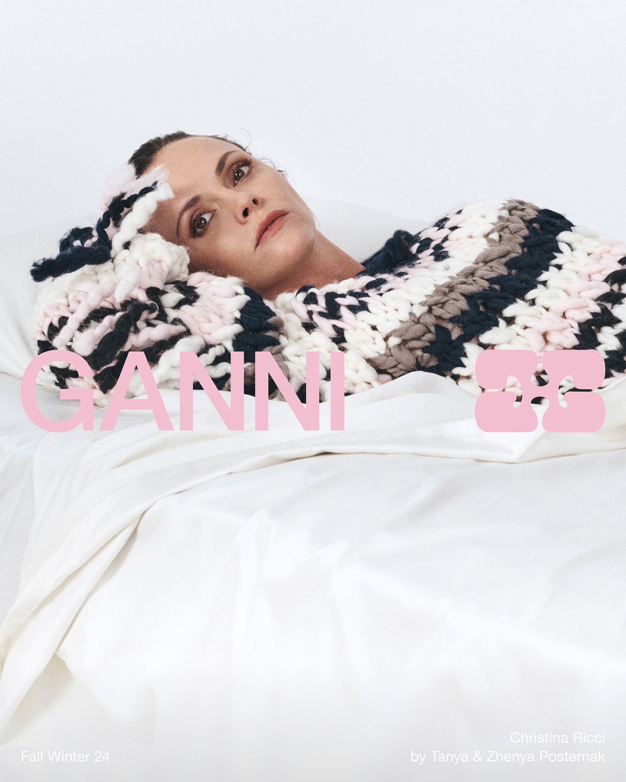Christina Ricci reclining on white sheets wearing a chunky knit sweater for Ganni Fall 2024 campaign