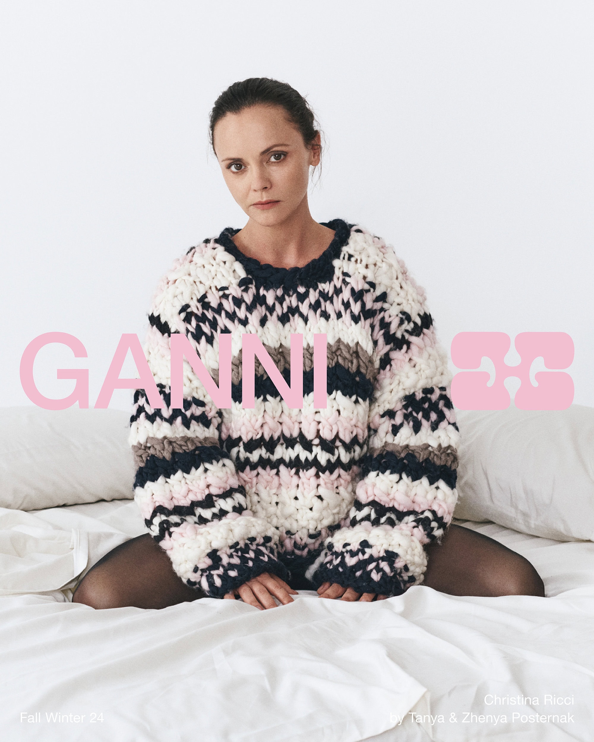 Christina Ricci wearing a chunky patterned sweater sitting on a white bed for Ganni Fall 2024 campaign
