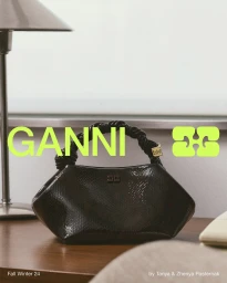 Black embossed leather handbag with a braided handle resting on a wooden desk next to a lamp for Ganni Fall 2024 campaign.