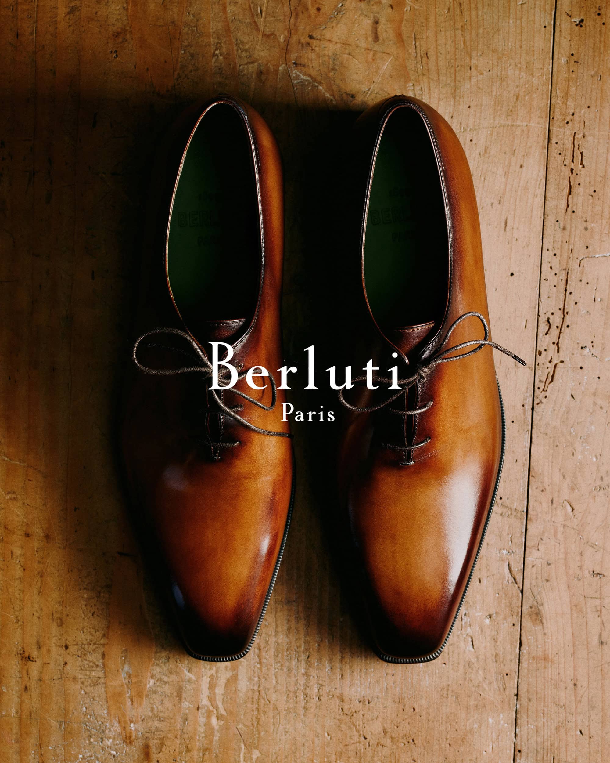 Top-down view of a pair of polished brown leather dress shoes on a wooden surface for Berluti Fall 2024 campaign