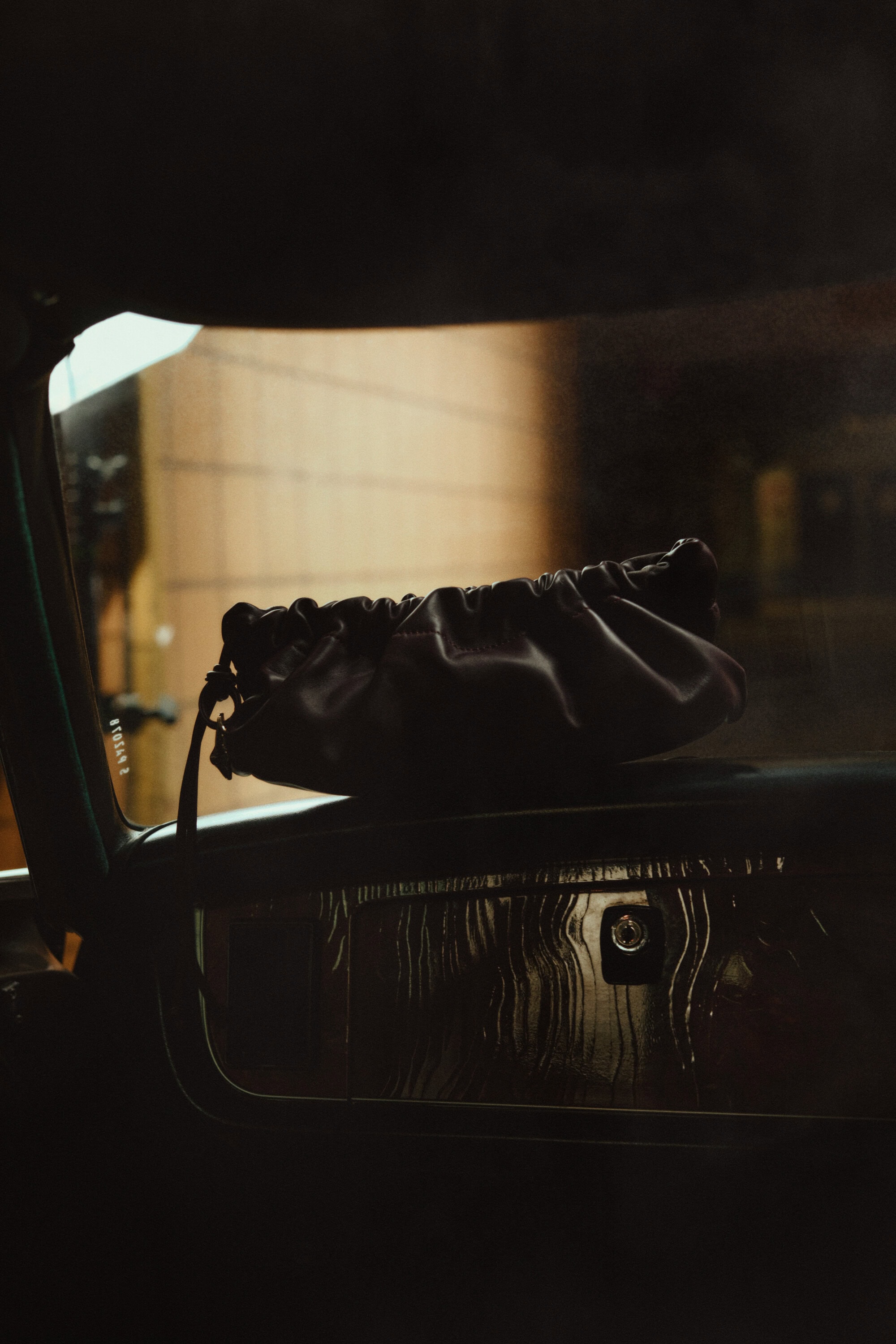 Dark leather handbag resting on the dashboard of a car interior with warm moody lighting.