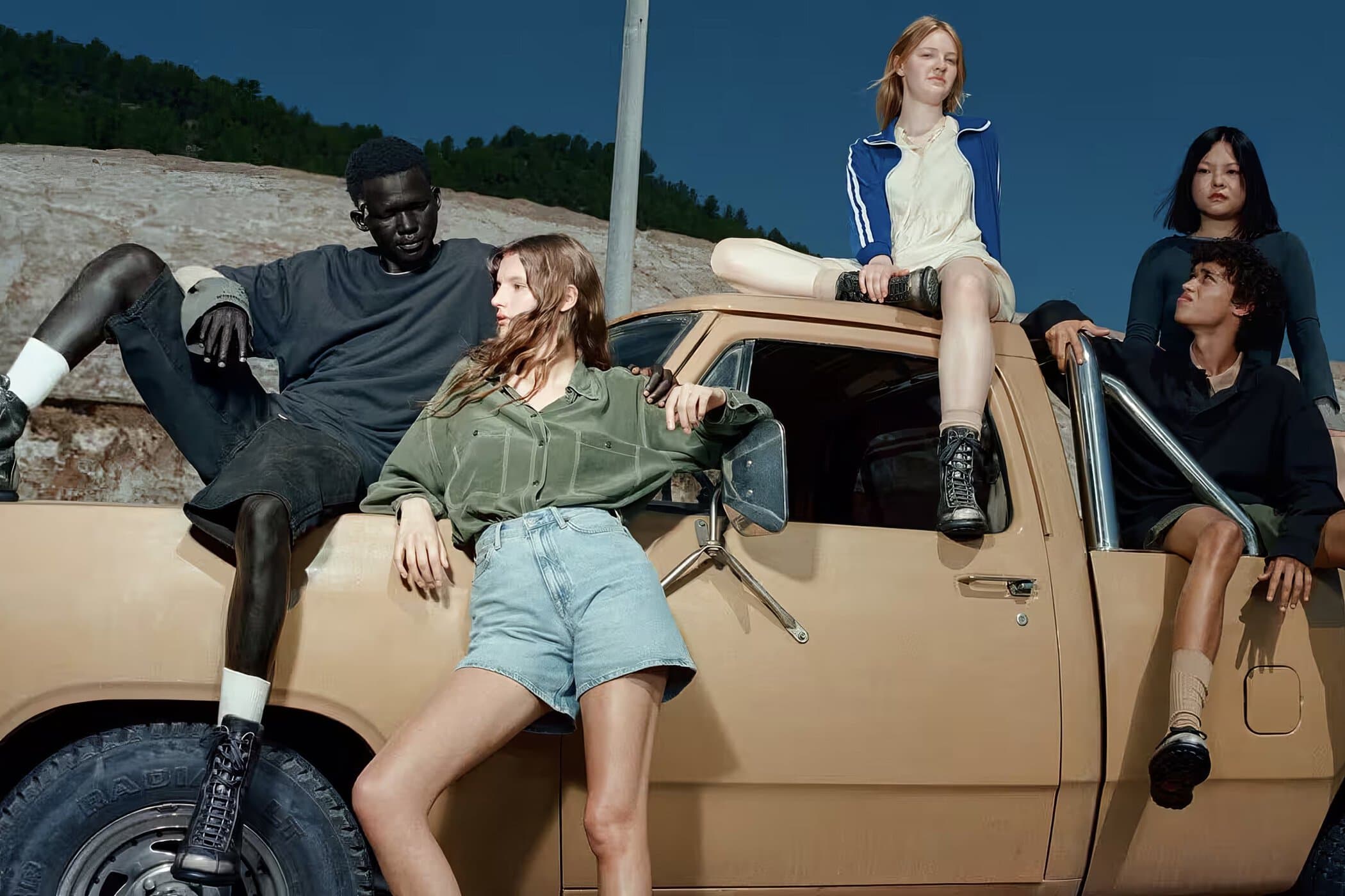 Five models posing on a vintage tan pickup truck against a blue sky for the Camper Fall 2024 campaign