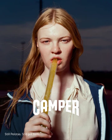 Close-up portrait of a red-haired woman holding an ice pop against an outdoor dusk sky for the Camper Fall 2024 campaign.