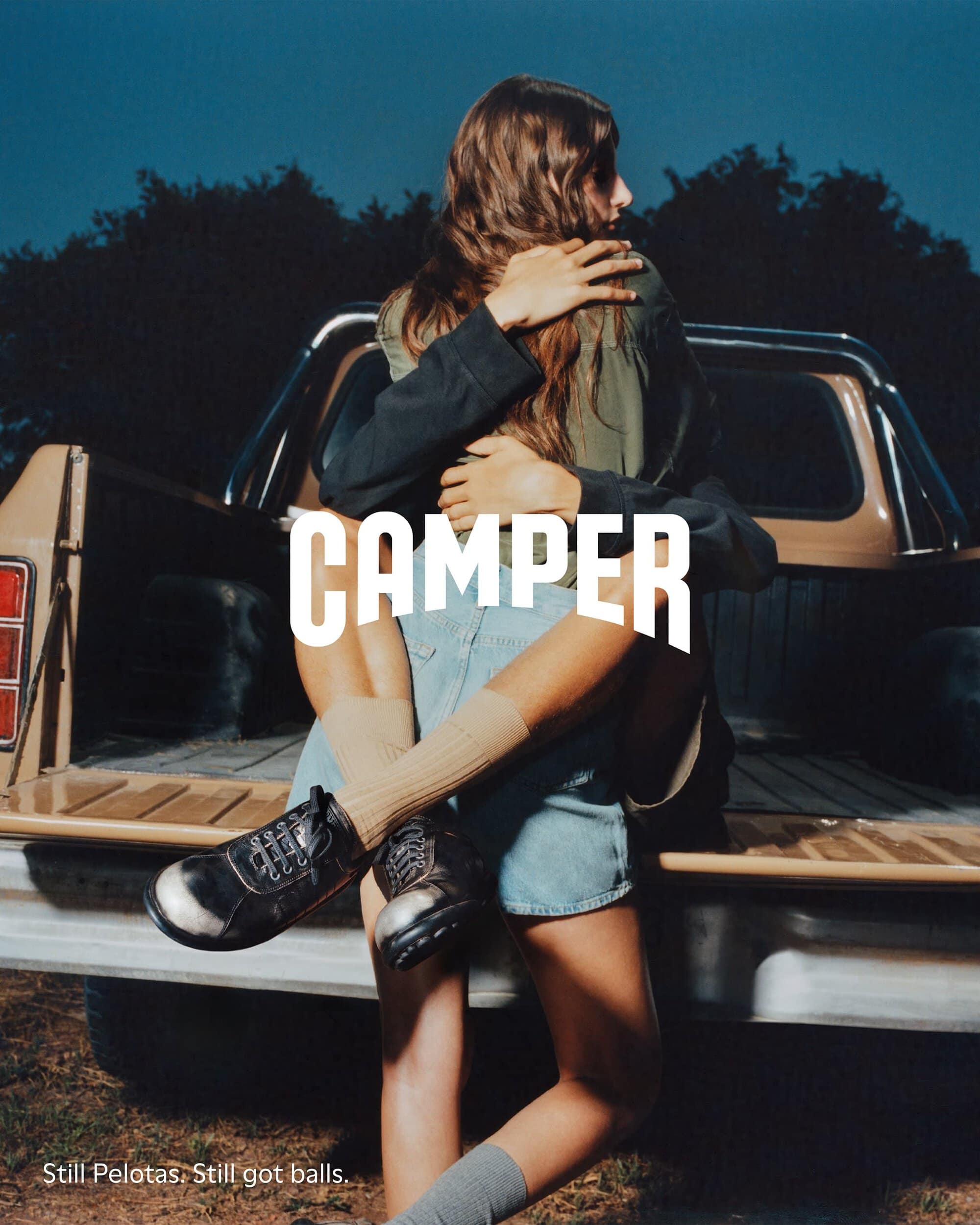 Two people embracing in front of a pickup truck wearing casual apparel and footwear