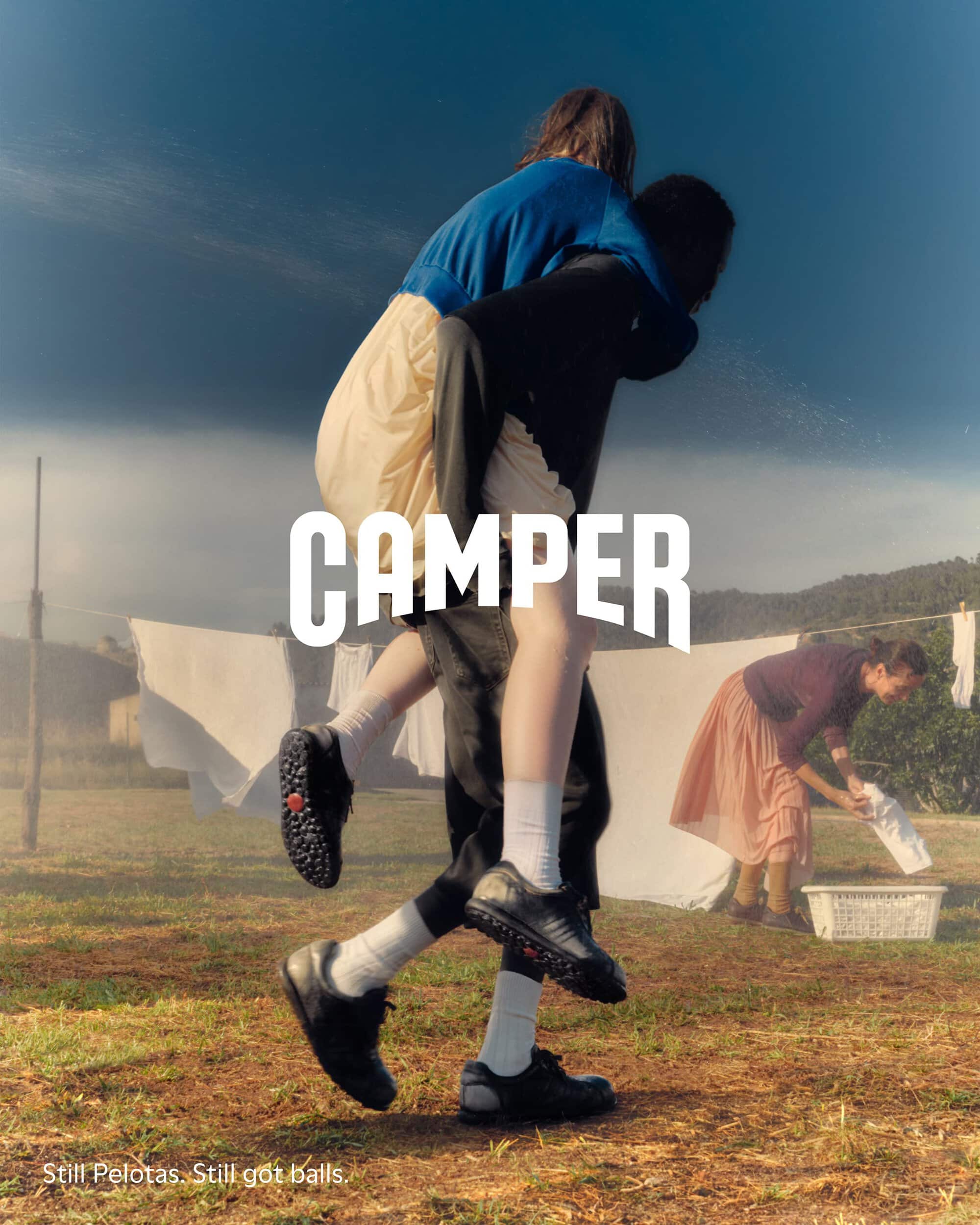 One person giving another a piggyback ride outdoors in a rural field with hanging laundry