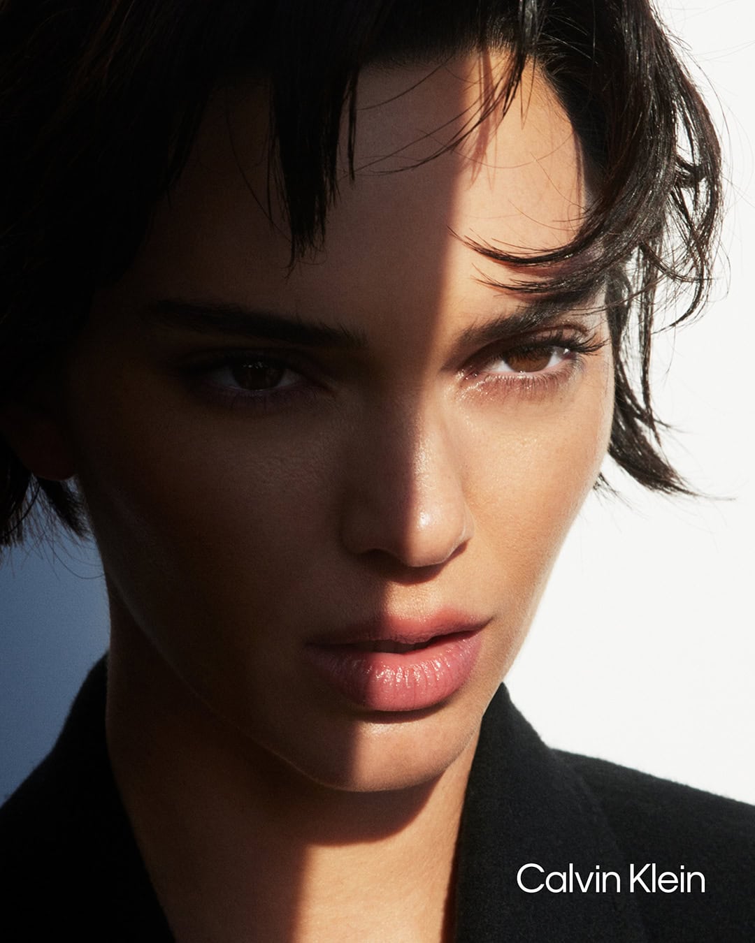 Close-up portrait of Kendall Jenner with dramatic lighting casting shadow across her face for Calvin Klein Fall 2024 campaign