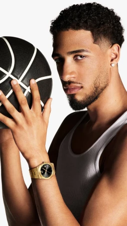 Tyrese Haliburton holding a black basketball wearing a white tank top and gold watch against a white seamless background