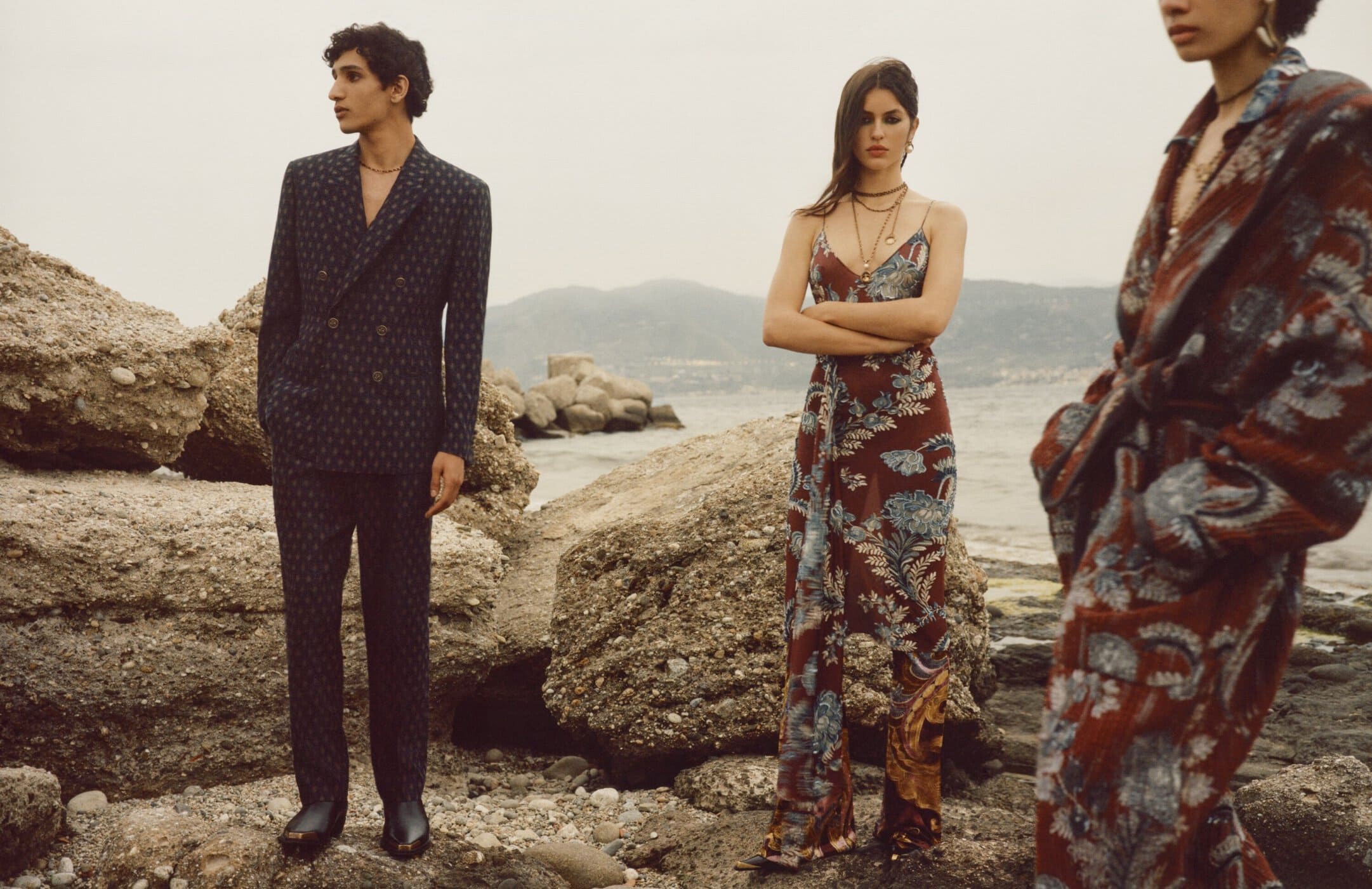 Three models posing near rocky shore and calm water for Etro Fall 2024 ad campaign photographed by Colin Dodgson.