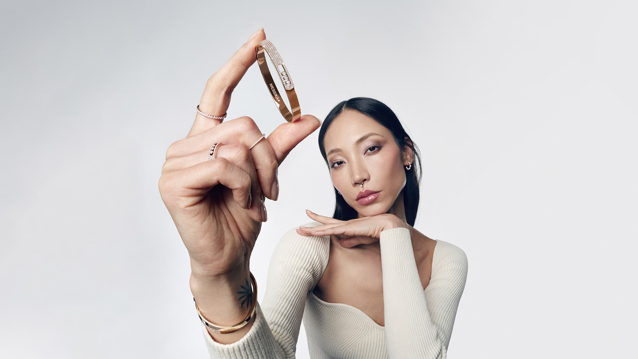 Model holding up a diamond-paved gold bangle bracelet in close-up against a clean white seamless studio background.