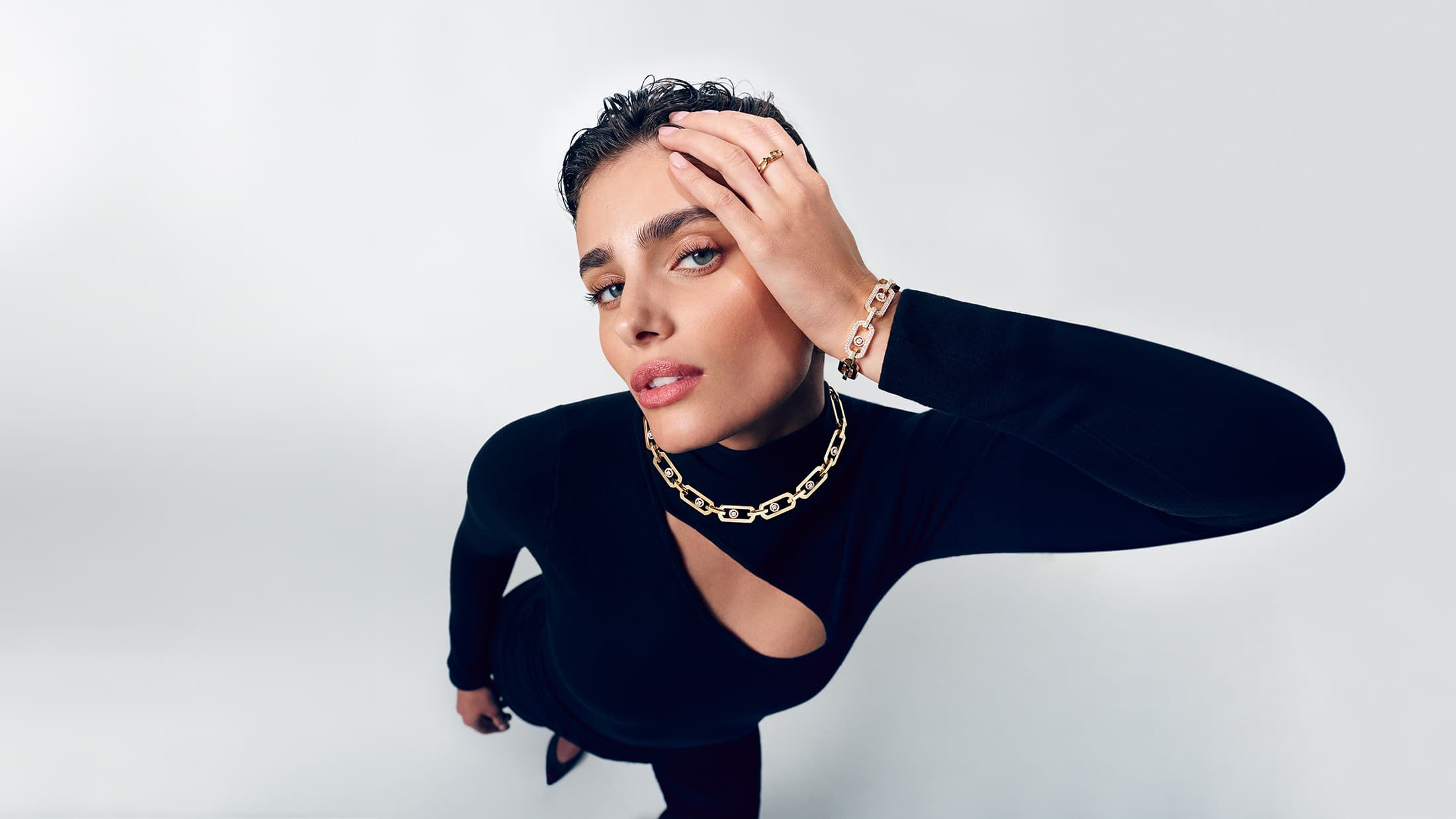 Model Taylor Hill wearing gold diamond jewellery and a black top against a white background for Messika