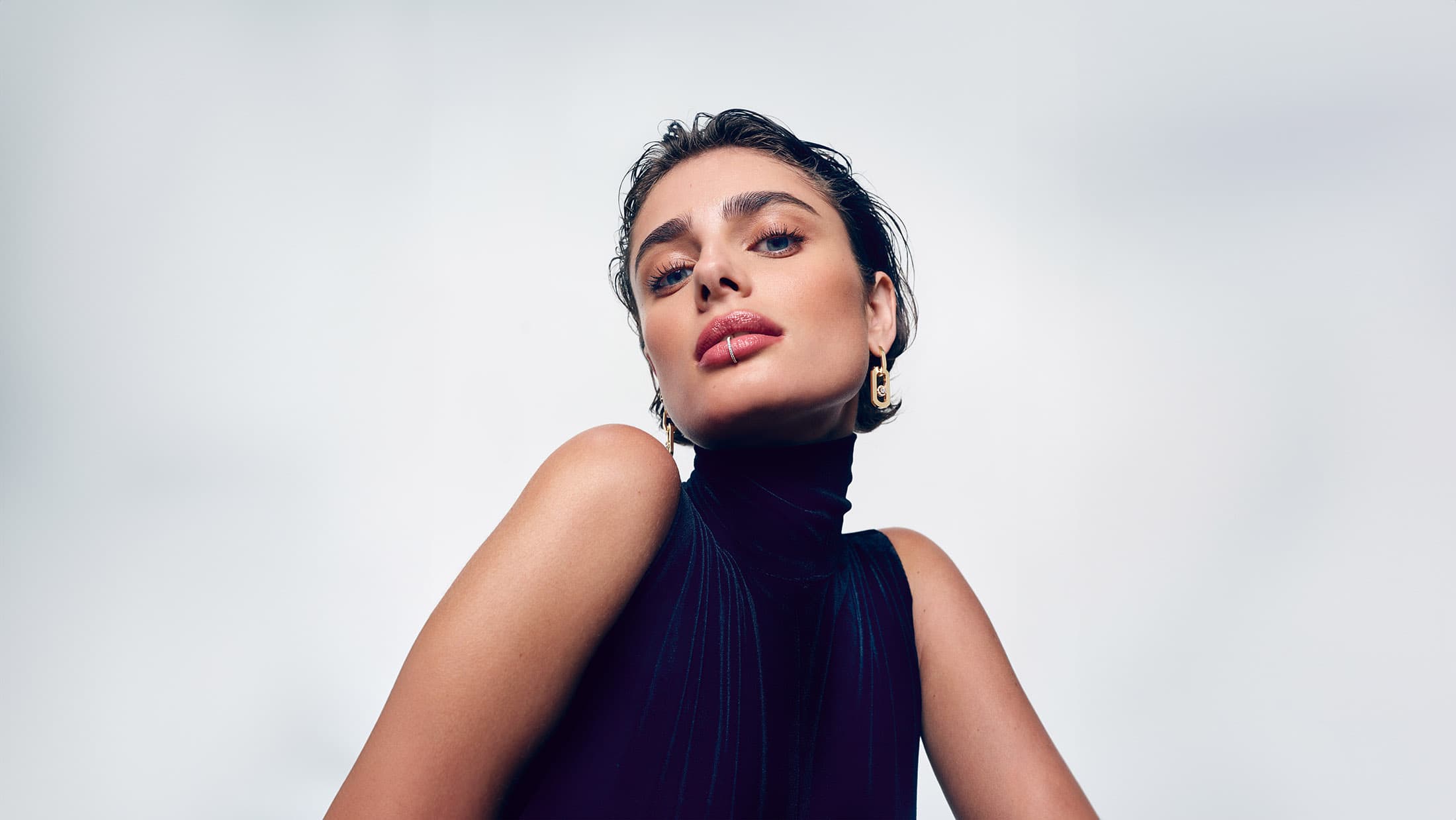 Model Taylor Hill wearing luxury jewellery and dark apparel against a plain studio background
