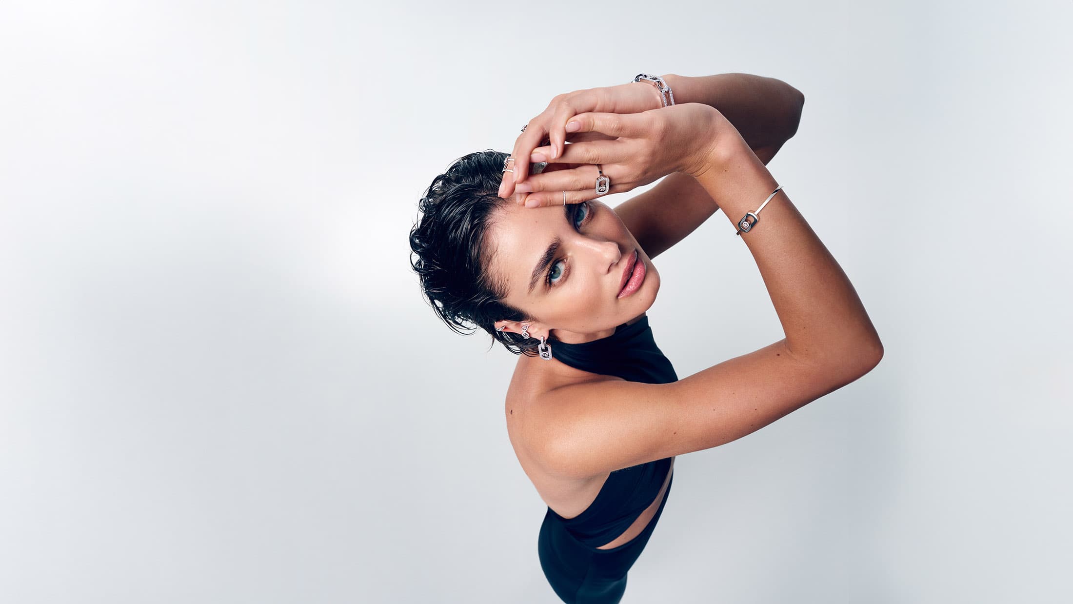 Model Taylor Hill with short dark wet-look hair posing against a plain white background wearing diamond jewellery and a black top