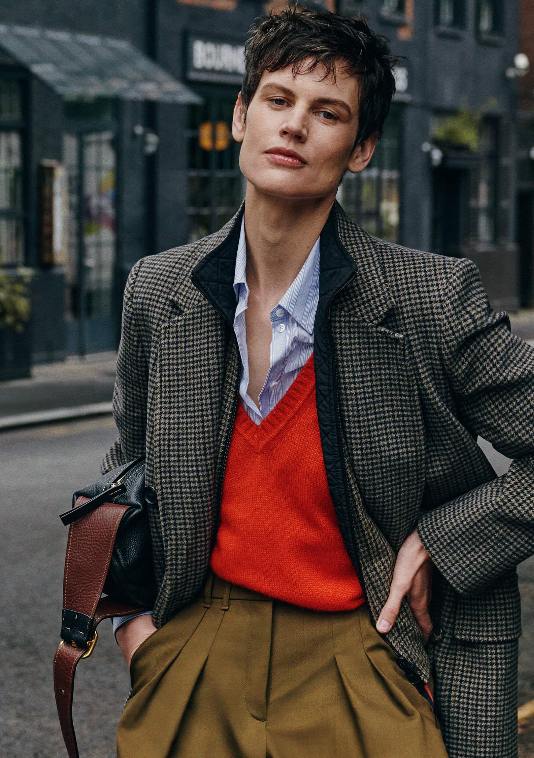 Model Saskia de Brauw in a houndstooth coat, red vest and olive trousers on a street for ME+EM
