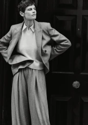 Model Saskia de Brauw in a grey blazer and trousers standing against a dark panelled door