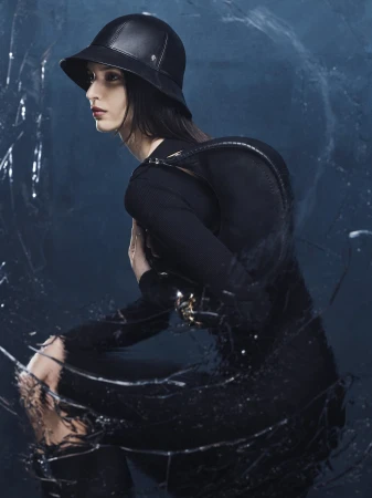 Model wearing a black leather hat and black top against a dark textured background