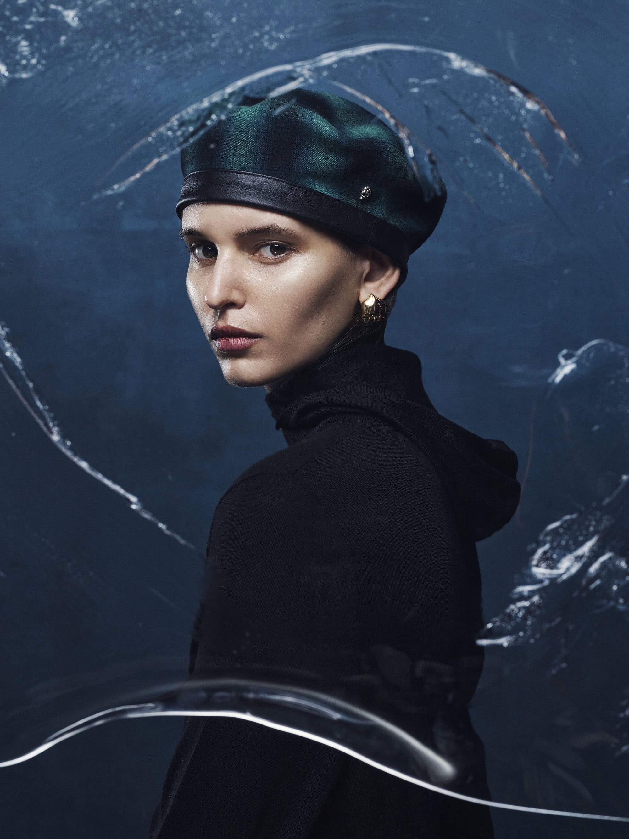 Model wearing a dark green plaid beret and black top behind textured glass for Helen Kaminski