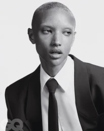 Model Georgia Palmer with a buzzcut wearing a black suit jacket, white shirt, and black tie against a white background for GQ Germany.