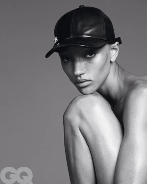 Model Georgia Palmer wearing a black leather baseball cap resting her chin on her knee in a black and white editorial portrait for GQ Germany.