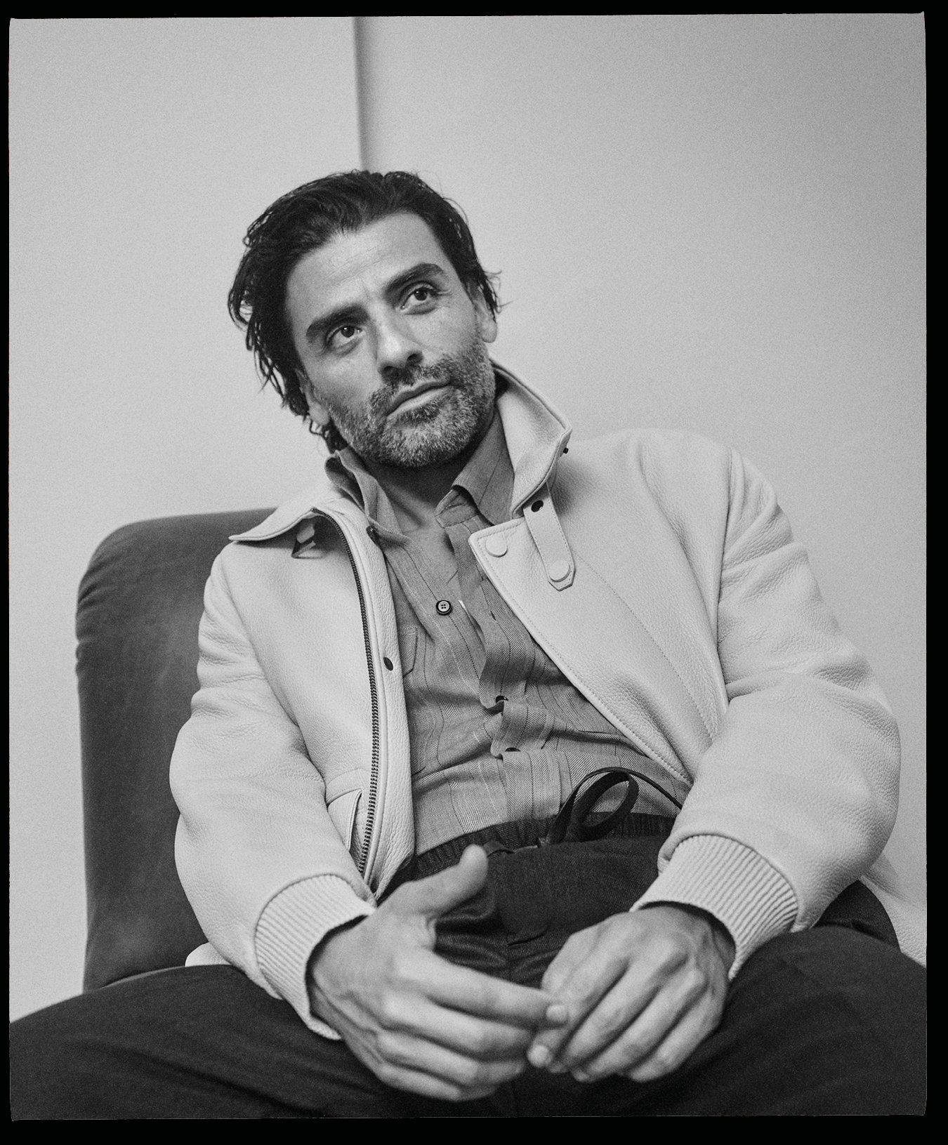Actor Oscar Isaac seated wearing a light jacket over a button-down shirt for the Brioni Fall 2024 campaign
