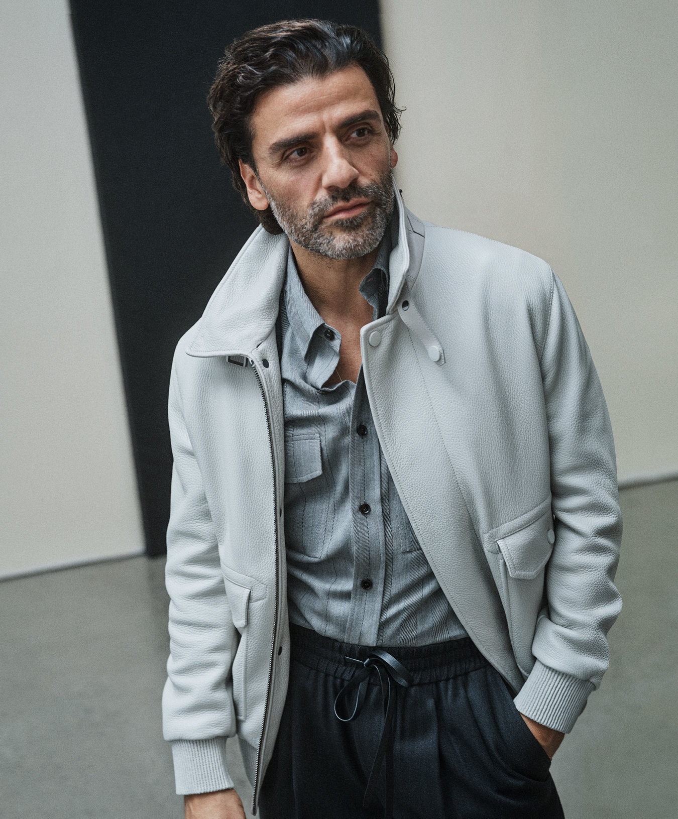 Oscar Isaac wearing an off-white jacket and grey shirt against a minimalist background for Brioni Fall 2024 campaign