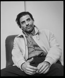 Actor Oscar Isaac seated wearing a light jacket over a button-down shirt for the Brioni Fall 2024 campaign