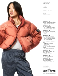 Peggy Gou wearing a rust orange puffer jacket against a solid white studio background.
