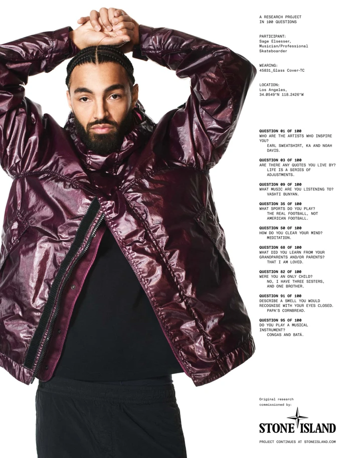 Man with braided hair and beard wearing a glossy dark purple hooded jacket against a white background