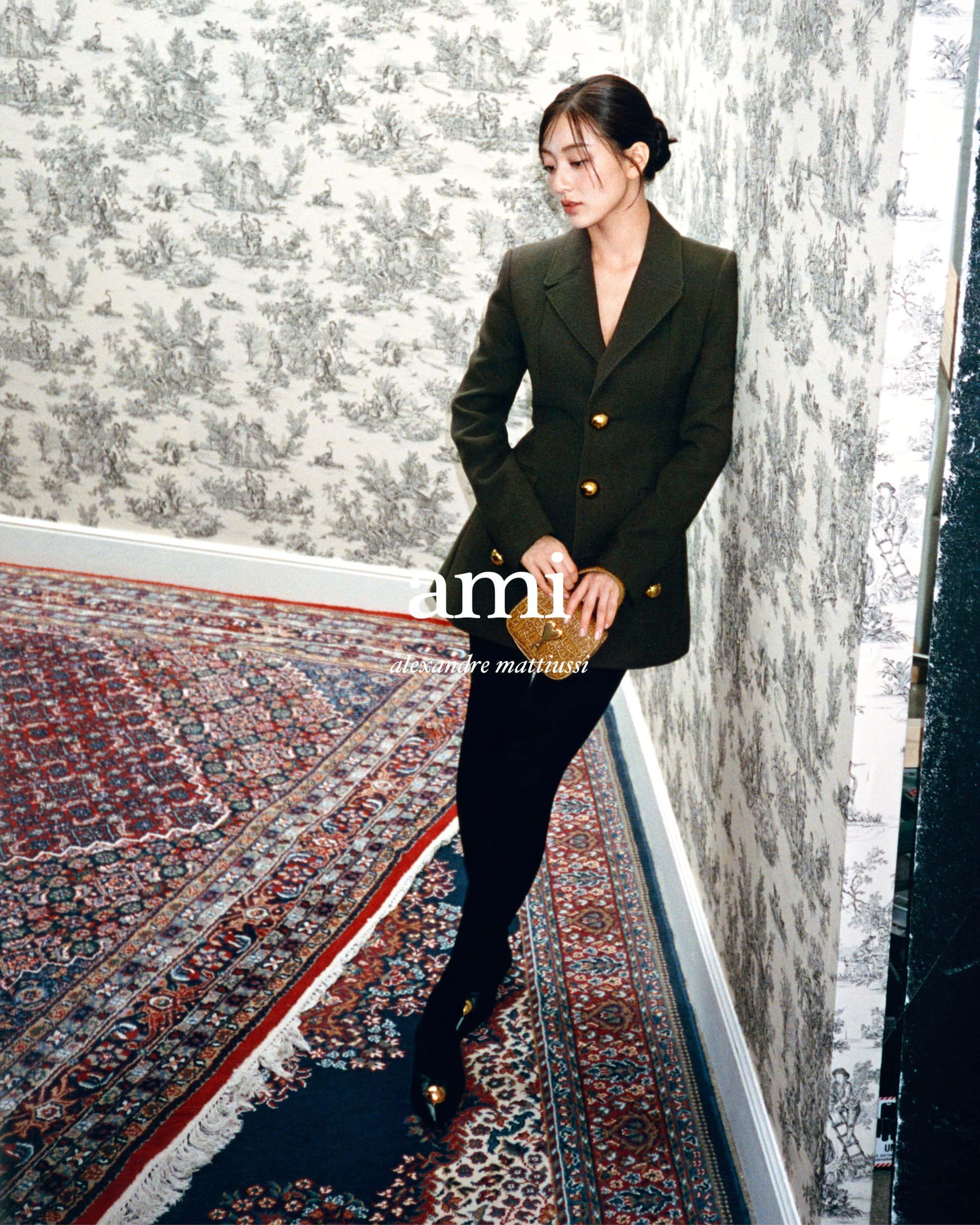 Model Jihyo leaning against a toile wallpaper wall wearing an olive green blazer and black tights for Ami